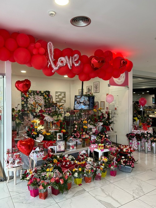 Flores vibrantes e arranjos temáticos para casamento, incluindo balões vermelhos em formato de coração e um letreiro escrito 'love'.
